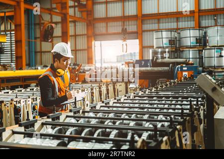 Junger männlicher Ingenieur, der die Qualitätskontrolle in der Metallblechherstellung durchführt und die Produktionslinie überprüft. Stockfoto