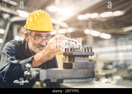 Leitender männlicher Ingenieur, der in der CNC-Drehmaschine in der Metallstahlfabrik mit hoher Qualifikation und Präzision arbeitet. Gesunde ältere Fräsmaschinen Stockfoto