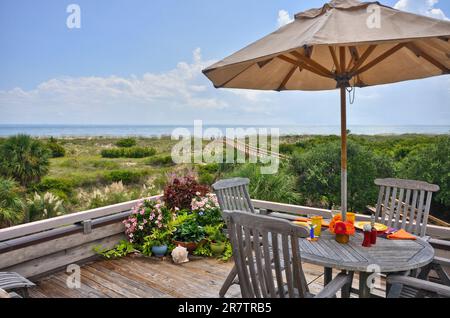 Ein Teakholz-Esstisch auf einer hölzernen Terrasse mit Blick auf die Dünen und ein Fußweg zum Strand - Tybee Island Georgia Stockfoto