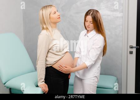 Arzt untersucht schwangere Frau während des Arztbesuchs, berührt ihren Bauch Stockfoto