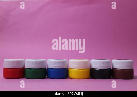 Farbe in Gläsern mit weißen Deckeln steht hintereinander, Turm auf rosafarbenem Hintergrund: Acryl Aquarell Öl Rot Gelb Blau Schwarz Weiß mit Platz für Text. Stockfoto