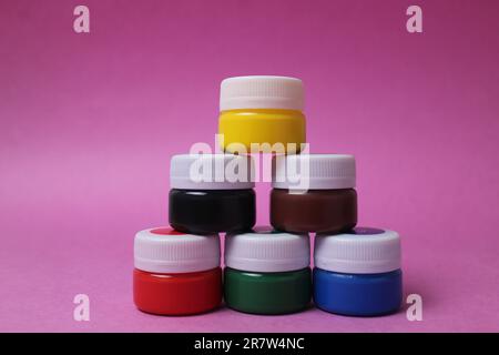Farbe in Gläsern mit weißen Deckeln steht hintereinander, Turm auf rosafarbenem Hintergrund: Acryl Aquarell Öl Rot Gelb Blau Schwarz Weiß mit Platz für Text. Stockfoto