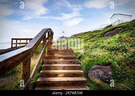 Holztreppe mit Geländer, die zu einem hohen weißen Leuchtturm führt, und historische Gebäude mit Blick auf den Atlantischen Ozean am Cape Spear Newfoundland Stockfoto