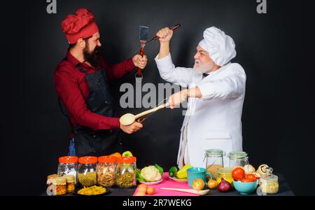 Zwei Köche streiten sich mit Küchenutensilien. Professionelles kulinarisches Angebot. Köche in Uniform konkurrieren in der kulinarischen Show. Kochwettbewerb. Kulinarische Schlacht Stockfoto