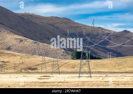 Foto von großen Übertragungstürmen und Linien, die durch ein Tal vor einem blauen Himmel auf der Südinsel Neuseelands verlaufen Stockfoto