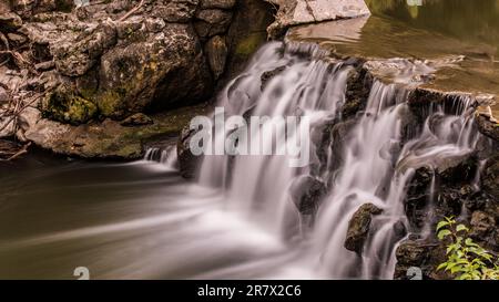 Ein langer Blick auf einen ruhigen Wasserfall, der sich über ein felsiges Gesicht hinunterschlängelt und von üppigem Grün umgeben ist Stockfoto