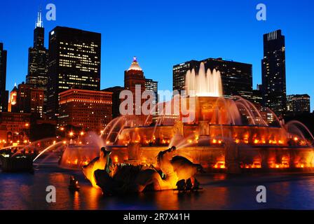 Der historische Buckingham Fountain im Grant Park ist in der Dämmerung beleuchtet und die Skyline von Chicago ist ebenfalls sichtbar Stockfoto