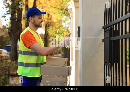 Kurier in Uniform mit Paketen, die draußen klingeln Stockfoto