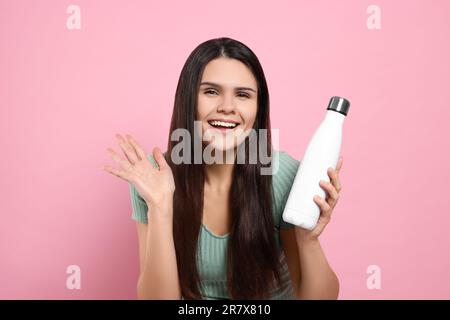 Junge Frau mit Thermoflasche auf pinkfarbenem Hintergrund Stockfoto
