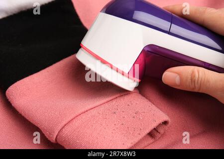 Frau, die einen modernen Stoffrasierer auf einem Pullover mit Fusseln und Nahaufnahme benutzt Stockfoto