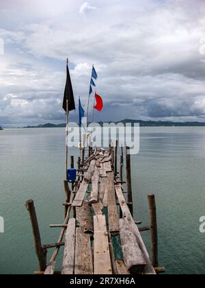 Hölzerne Fußgängerbrücke mit Flaggen in einem traditionellen Fischerdorf in Koh Lanta, Thailand. Stockfoto