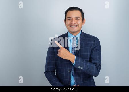 Junger Mexikaner mit brauner Haut, gekleidet als Unternehmer oder Geschäftsmann, zeigt glücklich mit dem Finger, eine Person Stockfoto