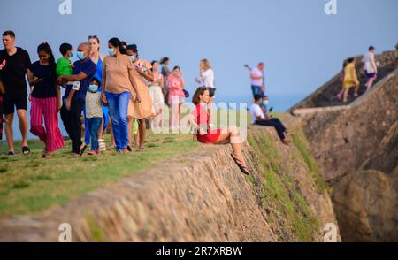 Galle, Sri Lanka - 02 15 2022: Süßes rot gekleidetes weißes Mädchen sitzt am Rand der Festungsmauer. Stockfoto