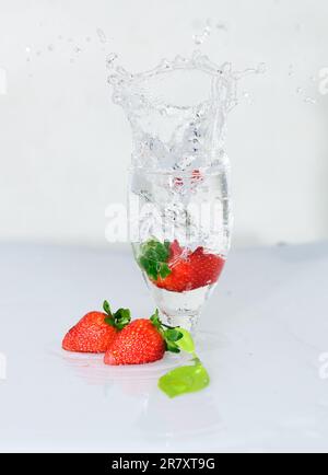 Erdbeerobst tropft auf ein Weinglas, gefrierende Bewegung des Wasserspritzers, weißer Hintergrund. Stockfoto