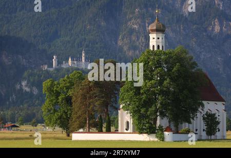 Schwangau, Deutschland. 18. Juni 2023. Schloss Neuschwanstein steht hinter der Wallfahrtskirche St. Kolumaner im Morgenlicht. In einem Referendum am Sonntag sollen die Bewohner Schwangaus entscheiden, ob sie die Nominierung von Neuschwanstein zum Weltkulturerbe unterstützen. Kredit: Karl-Josef Hildenbrand/dpa/Alamy Live News Stockfoto