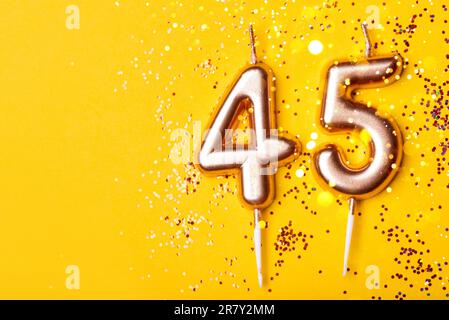 45 Jahre Feier. Grußbanner. Goldene Kerzen in der Form der Nummer 45 auf gelbem Hintergrund mit Konfetti. Stockfoto