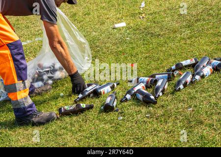 München, Deutschland. 18. Juni 2023. Ein Mitarbeiter der Stadtwerke räumt den Müll auf, der von Besuchern des Vortags und Nachts auf dem großen Rasen im Englischen Garten in großen Mengen zurückgelassen wurde. Dutzende Bier- und Weinflaschen, zerbrochenes Glas, Snacktaschen und anderer Müll liegen im Freien herum. Im Hintergrund sind die bereits gebackenen Müllsäcke zur Entnahme bereit. Kredit: Peter Kneffel/dpa/Alamy Live News Stockfoto