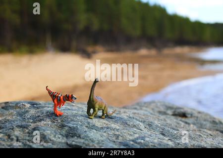 Zwei Spielzeugdinosaurier auf einem Felsen am Strand. Stockfoto