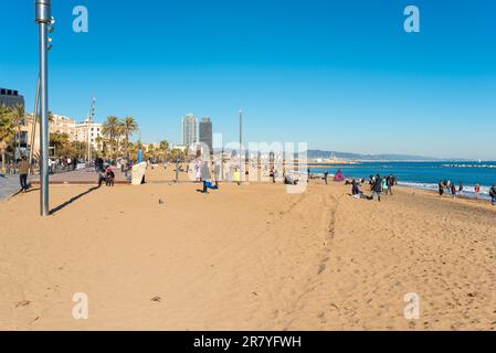 Leute, die auf der Platja de Sant Sebastia sitzen, Means, dem Strand von Barceloneta in Barcelona. Die Promenade ist bei den Einheimischen sehr beliebt Stockfoto