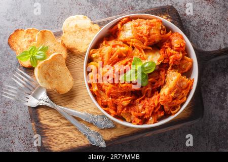 Hausgemachter Fischeintopf mit Gemüse in scharfer Tomatensauce, serviert mit Toast, Nahaufnahme auf einem Holzbrett auf dem Tisch. Horizontale Draufsicht von oben Stockfoto