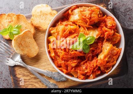 Köstlicher Fischeintopf mit Gemüse in scharfer Tomatensauce, serviert mit Toast, Nahaufnahme auf einem Holzbrett auf dem Tisch. Horizontale Draufsicht von oben Stockfoto