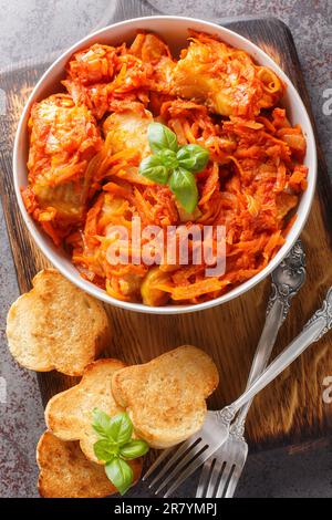 Weißes Fischfilet mit Karotten, Zwiebeln und Sellerie in Tomatensoße serviert mit Toast aus nächster Nähe auf einem Holzbrett auf dem Tisch. Vertikale Draufsicht Stockfoto