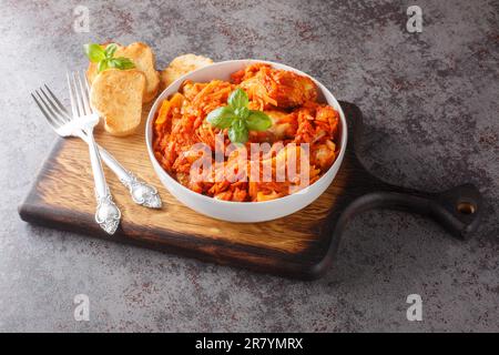 Weißer Fischeintopf mit Karotten und Zwiebeln in scharfer Tomatensoße serviert mit Toast aus nächster Nähe auf einem Holzbrett auf dem Tisch. Horizontal Stockfoto