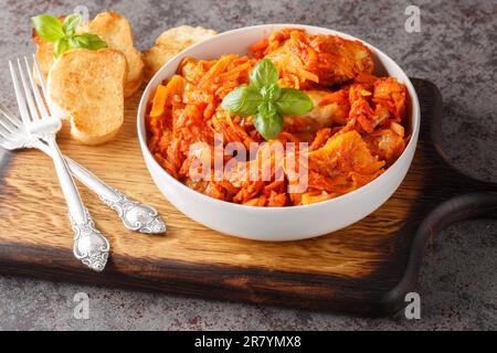 Hausgemachter Fischeintopf mit Gemüse in scharfer Tomatensauce, serviert mit Toast, Nahaufnahme auf einem Holzbrett auf dem Tisch. Horizontal Stockfoto