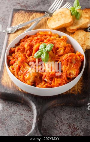 Weißes Fischfilet mit Karotten, Zwiebeln und Sellerie in Tomatensoße serviert mit Toast aus nächster Nähe auf einem Holzbrett auf dem Tisch. Vertikal Stockfoto