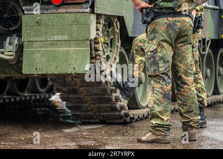 Zwei Soldaten in Tarnuniform standen während einer Pause unter dem Regen neben den Schienen eines gepanzerten Panzers, nur die Hosen und die Stiefel Stockfoto