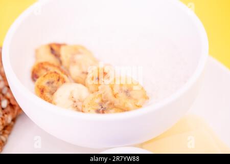 Reisbrei auf Kokosmilch mit Bananen in einer Schüssel auf gelbem Hintergrund, in einem Café Stockfoto