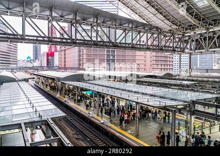 Blick von oben auf die Bahnsteige am Bahnhof Osaka in Japan. Schlangen von Fahrgästen in den ausgewiesenen Räumen, je nach gewünschtem Zugtyp. Stockfoto