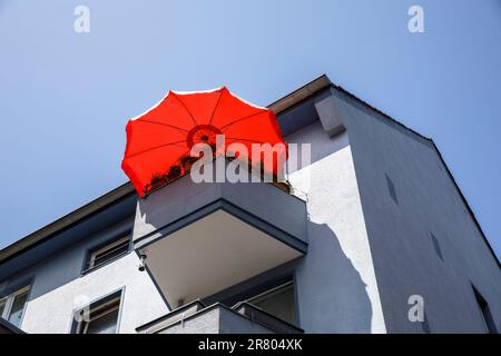 Roter Sonnenschirm auf dem Balkon eines grauen Wohnhauses in der Ursulagarten Straße, Köln. roter Sonnenschirm auf einem Balkon eines grauen Wohnha Stockfoto