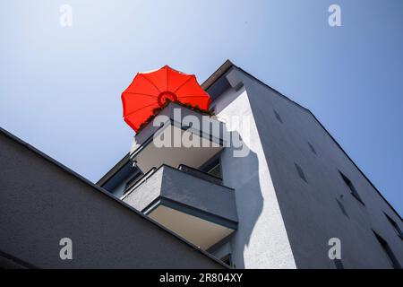 Roter Sonnenschirm auf dem Balkon eines grauen Wohnhauses in der Ursulagarten Straße, Köln. roter Sonnenschirm auf einem Balkon eines grauen Wohnha Stockfoto