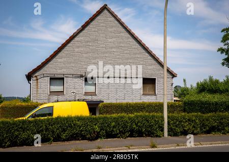 Ein gelbes Auto steht hinter einer Hecke vor einem grauen Ziegelhaus in Gevelsberg-Silschede, Nordrhein-Westfalen, Deutschland. Ein gelbes Auto Stand Tipp Stockfoto