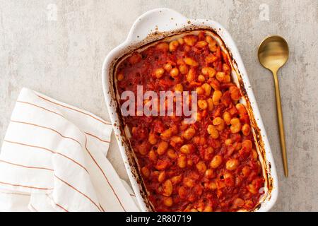 Gesundes Frühstück und Mittagessen, gedünstete weiße Bohnen mit Karotten, Zwiebeln und Tomaten, Blick von oben auf eine ovale Keramikrösterei mit gedünsteten Hülsenfrüchten Stockfoto