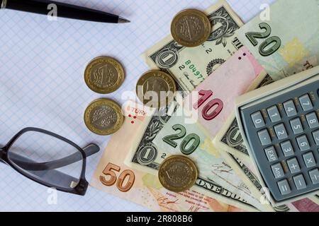 Türkisches Geld, Banknoten und US-Dollar auf dem karierten weißen Papier mit Stift, Brille, Smartphone, Münzen und Taschenrechner. Stockfoto