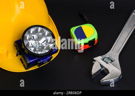 Gelber Schutzhelm, Helm, Deckenleuchte, Maßband und Schraubenschlüssel auf schwarzer Oberfläche, über der Ansicht Stockfoto