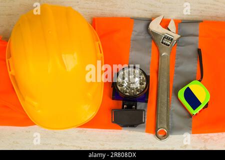 Gelber Schutzhelm, Helm, Deckenleuchte, Maßband und Schraubenschlüssel auf reflektierender Arbeitsweste Stockfoto