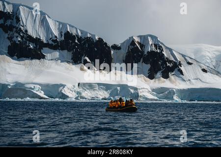 Antarktis-Expedition, Kreuzfahrtpassagiere in gelben Parkas, Fahrt in einem aufblasbaren Zodiac-Boot, sehr nah an einem riesigen weißen Eisberg. Klimawandel und Stockfoto