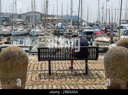 Ein Gentleman entspannt sich auf einer Bank mit Blick auf den Yachthafen am North Quay im Hafen von Plymouth in Sutton. Jetzt sehr viel und gehobene Wohngegend mit Som Stockfoto