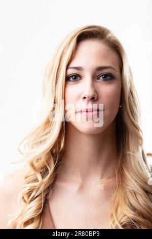 Das frontseitige Porträt einer selbstbewussten blonden Frau. Ihr stummes Lächeln scheint durch ihre Augen. Weißer Hintergrund verstärkt ihren Glanz Stockfoto
