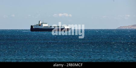 Tinos Island, Kykladen, Ziel Griechenland. Containerfrachtschiff kommt im Hafen an, glitzerndes Ägäisches Meer, blauer Himmel Hintergrund. Leerzeichen Stockfoto