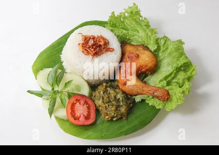 Galangal gebratenes Hähnchen, Reis, Sambal, Tomaten, Gurke, Basilikum, Salat. Indonesische Küche auf Bananenblatt-Teller. Knusprig gebratenes Hähnchen und grüner Sambal Stockfoto