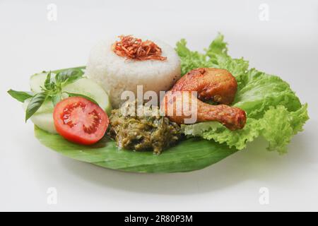 Galangal gebratenes Hähnchen, Reis, Sambal, Tomaten, Gurke, Basilikum, Salat. Indonesische Küche auf Bananenblatt-Teller. Knusprig gebratenes Hähnchen, grünes Chili Sambal Stockfoto