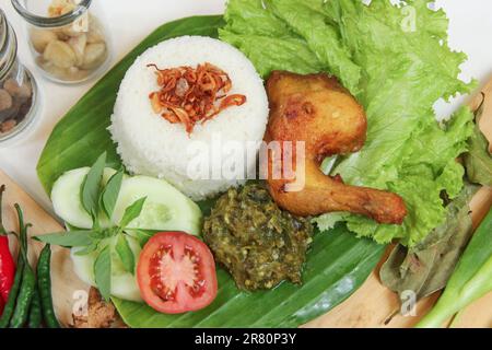 Galangal gebratenes Hähnchen, Reis, Sambal, Tomaten, Gurke, Basilikum, Salat. Indonesische Küche auf Bananenblatt-Teller. Knusprig gebratenes Hähnchen, grünes Chili Sambal Stockfoto