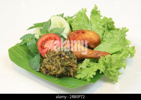 Galangal gebratenes Hähnchen, Sambal, Tomate, Gurke, Basilikum, Salat. Indonesische Küche auf Bananenblatt-Teller. Gastronomie-Fotografie auf weißem Hintergrund Stockfoto