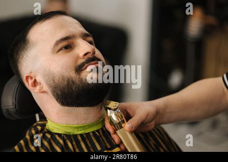 Nahaufnahme des professionellen Barbertrimmens, um den Bart des Kunden zu erhalten. Ein gutaussehender bärtiger Mann im Friseursalon Stockfoto