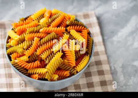 Rohe Fusilli-Pasta auf Beton. Dreifarbige Rotini- oder Fusilli-Pasta auf einer Leinenserviette. Italienisches Essen Stockfoto