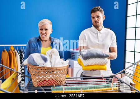 Hispanische Mutter und Sohn hängen Kleider an der Wäscheleine, ahnungslos und verwirrter Ausdruck. Zweifelhaftes Konzept. Stockfoto